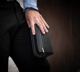Man Carrying Leather Wrist Bag from Rydal in 'Black'.