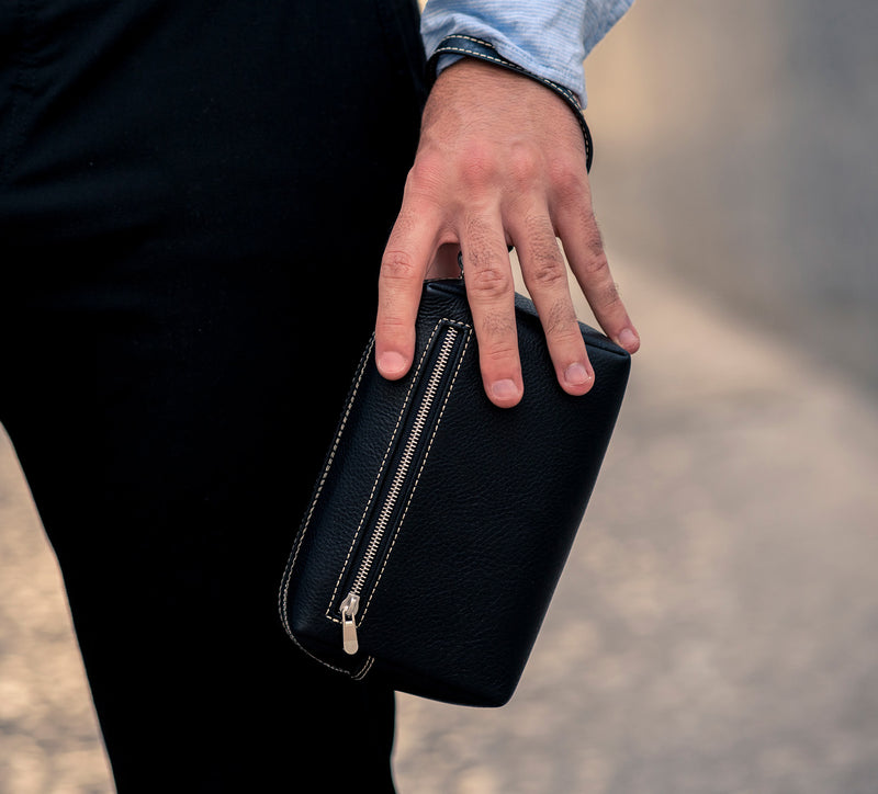 Man Gripping Leather Wrist Bag from Rydal in 'Black'.