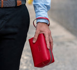 Man Holding Leather Wrist Bag from Rydal in 'Red'.