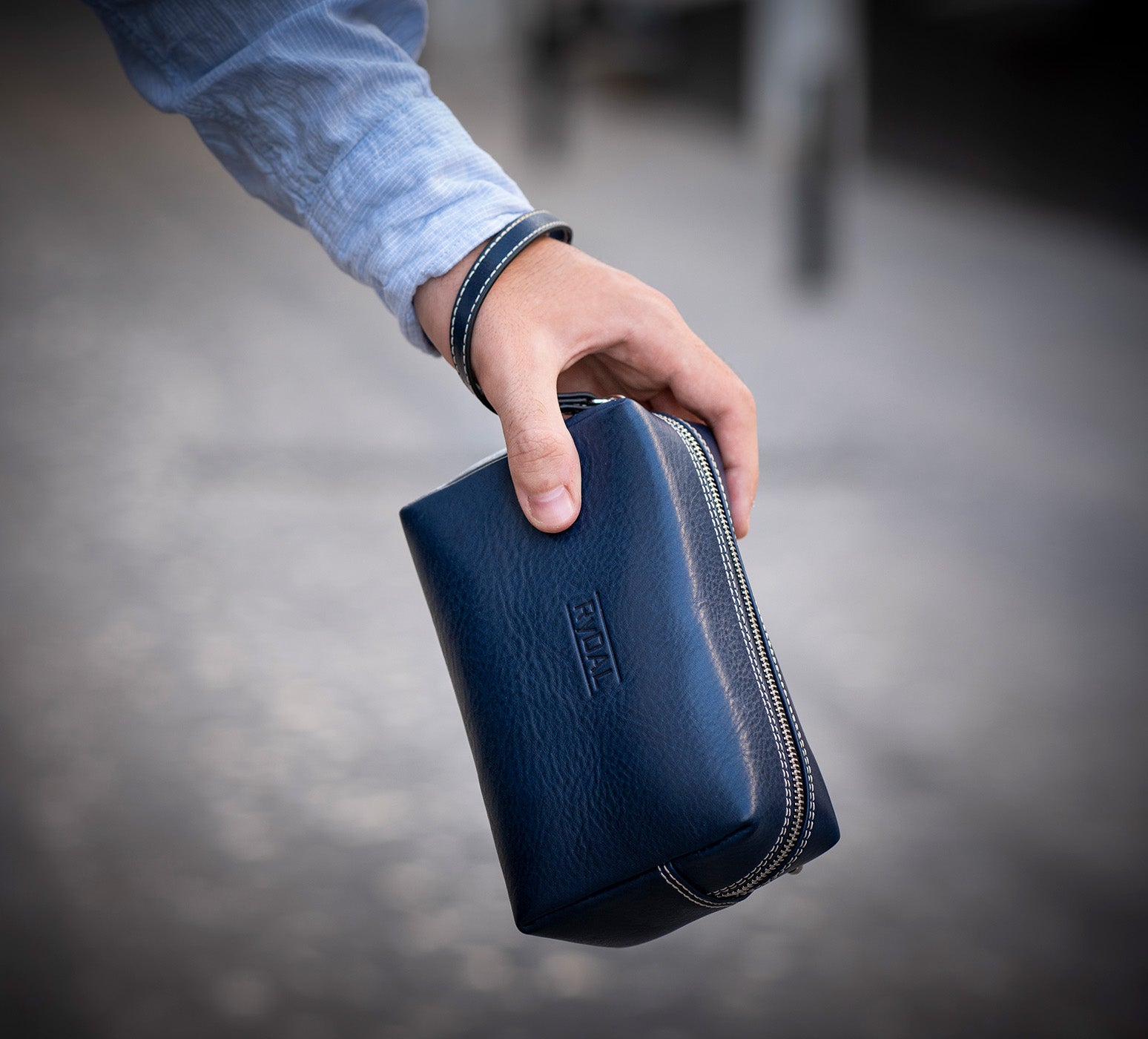 Man Clasping Leather Wrist Bag from Rydal in 'Royal Blue'.